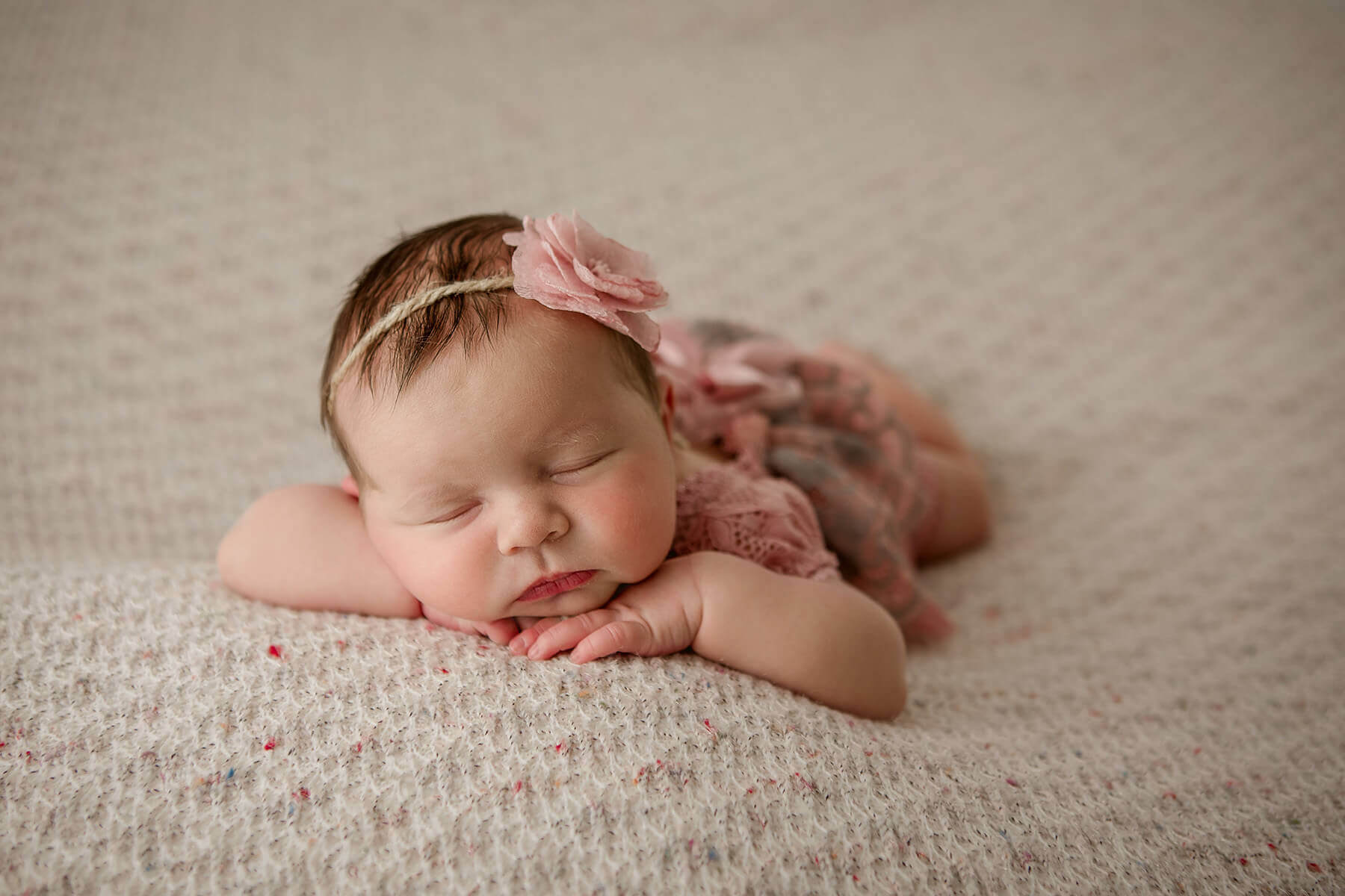 A baby girl sleeps resting her head on her hands on her tummy in a pink dress on a bed after meeting pediatric dentists in champaign il