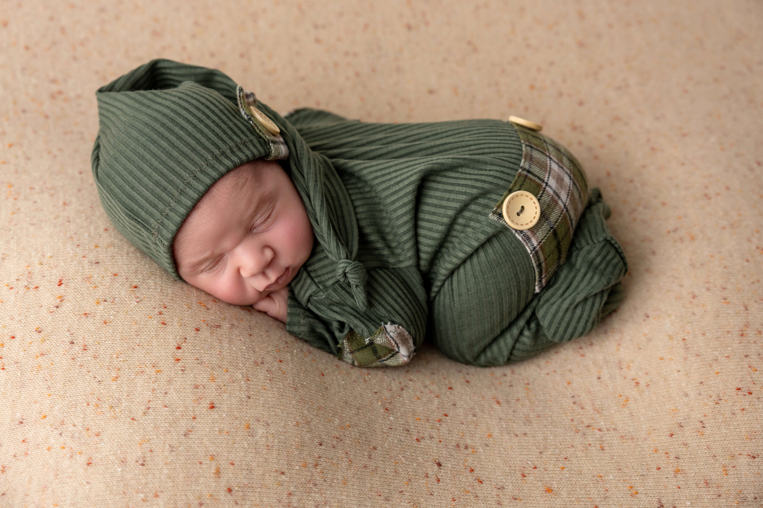 A newborn sleeps in green pajamas and matching sleep cap on a pad after meeting a doula in champaign, il