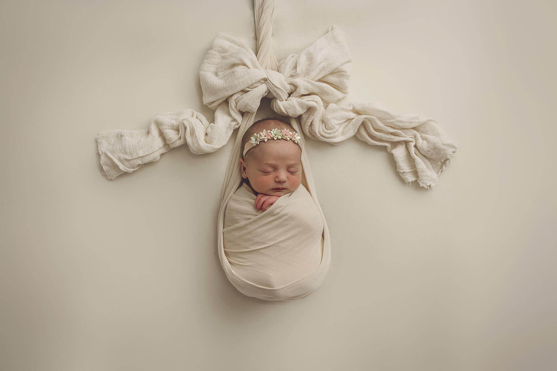 A sleeping newborn in a white swaddle with a bow over her on a bed thanks to here together birth