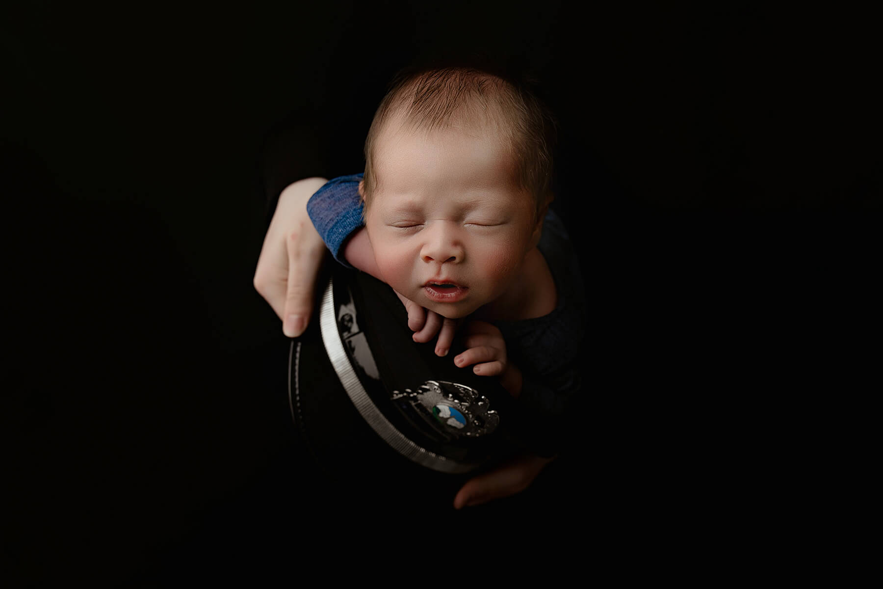 A newborn baby sleeps on a military cap held by mom in a studio after enjoying a pediatric chiropractors in Champaign, IL