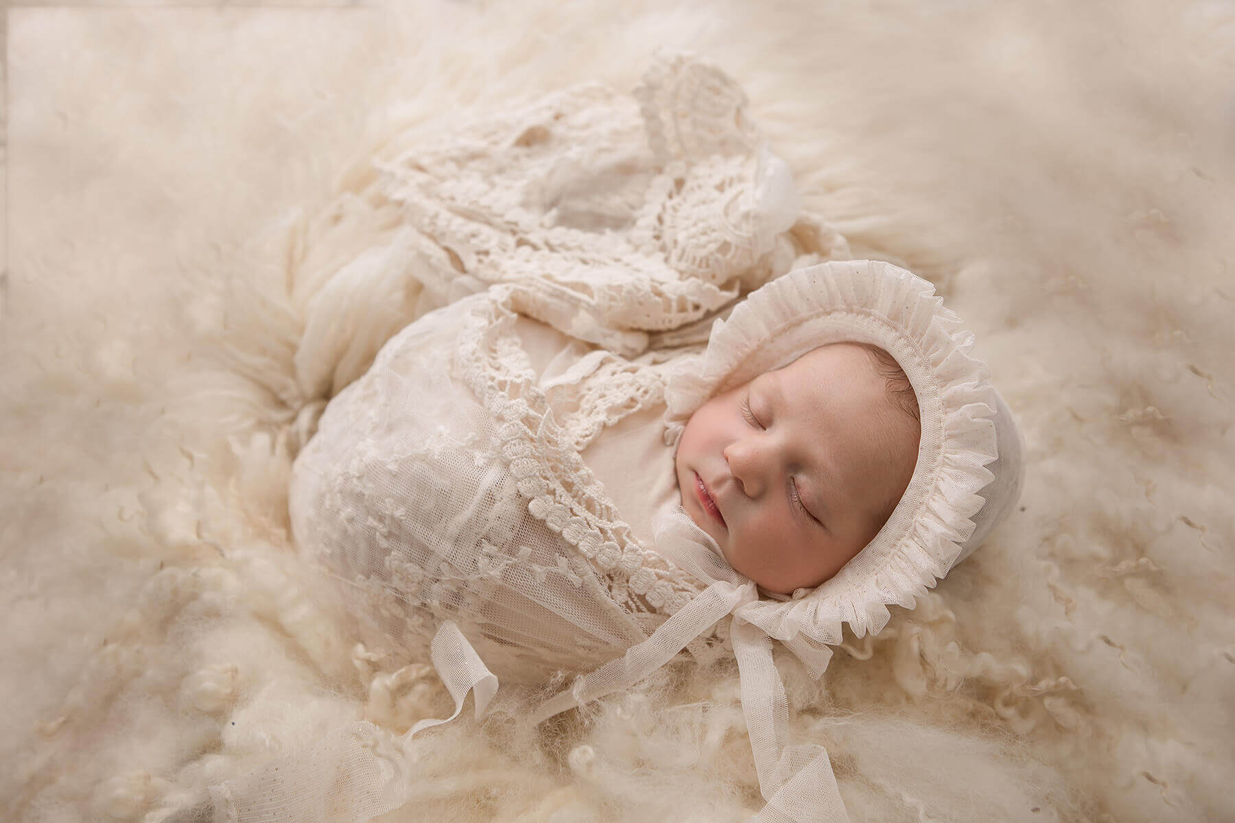 A newborn baby sleeps in a white swaddle and bonnet covered in lace in a fluffy blanket after mom enjoyed placenta encapsulation in Champaign, IL