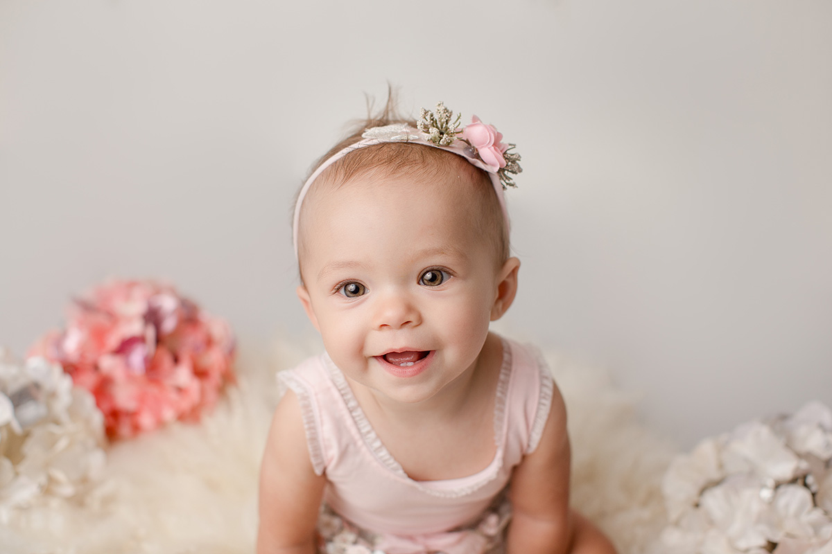 A closeup of a baby girl in a pink dress smiling with a matching flower headband