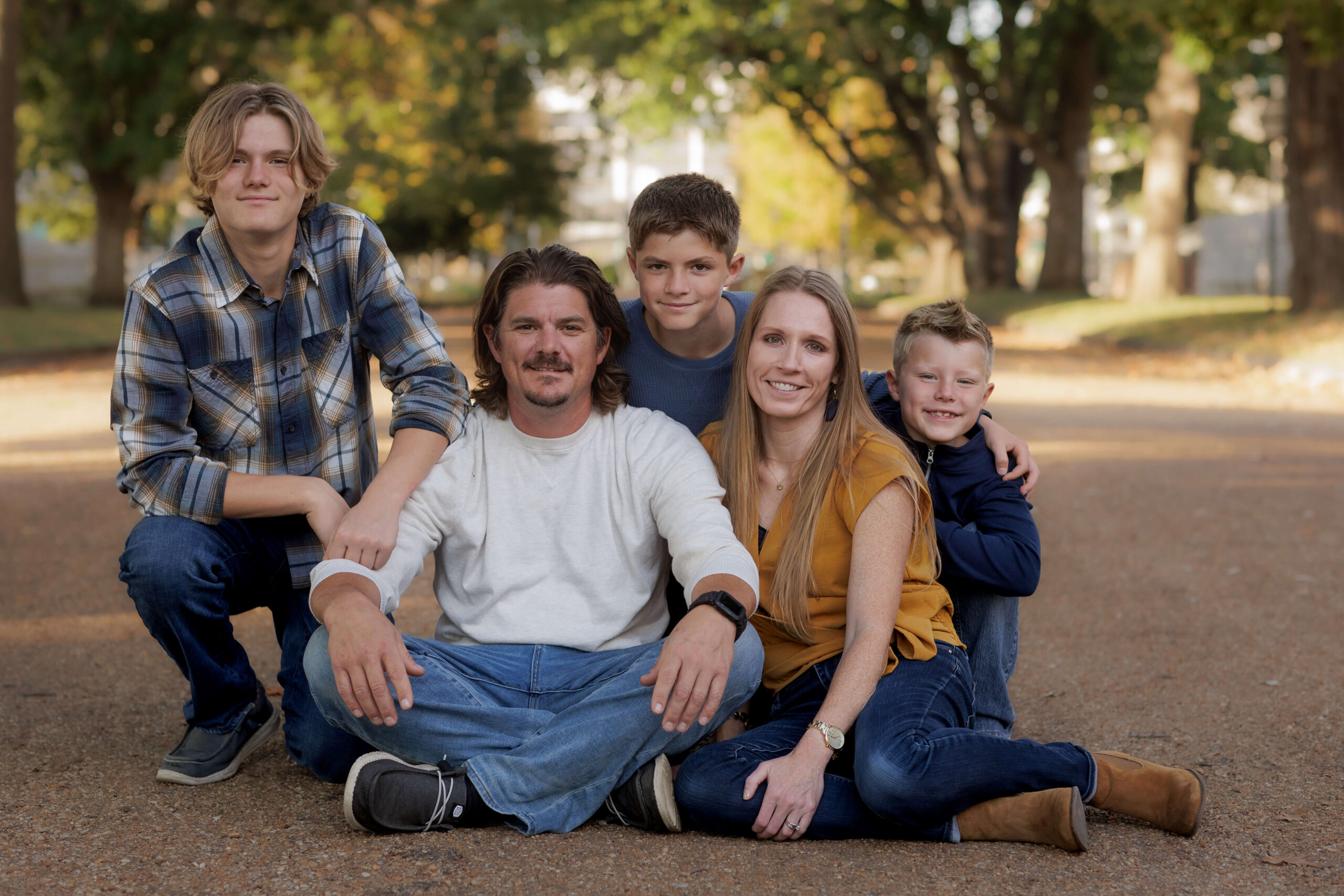 A mom and dad sit in a park path in front of their smiling and kneeling three sons in blue outfits before some fall activities in Peoria, IL